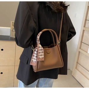 Close-up of brown litchi pattern leather bucket bag with decorative plaid scarf handle