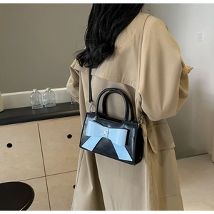 Detail of crossbody bag featuring a matte black finish and large blue bow with heart buckle