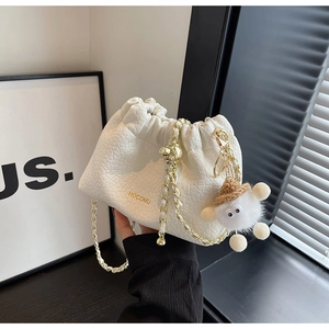 Detail of white crocodile texture bucket bag with gold chain and cute plush monster charm