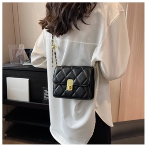 Detail of black quilted leather crossbody bag with gold chain strap and spherical buckle