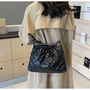 Detail of black quilted bucket bag with chain strap shown on a tan trench coat