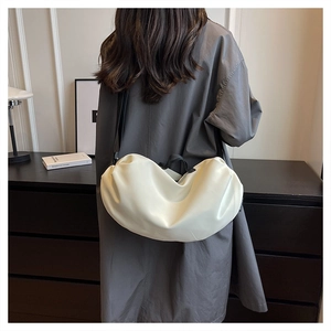Detail of off-white pleated dumpling bag with black straps worn by model at home