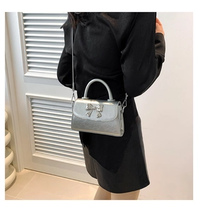 Close-up of metallic silver crossbody bag with a 3D bow buckle shown on a model