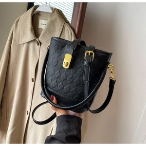 Détail du sac seau en cuir noir avec texture matelassée et fermoir doré sur trench beige