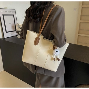 Detail of a large cream tote bag with brown leather straps and a plush toy charm