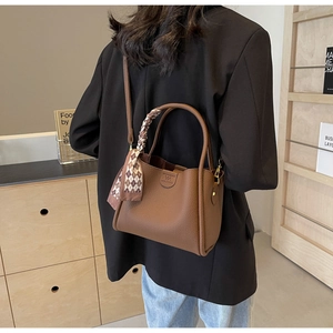 Brown litchi leather bucket bag shown on shoulder with silk scarf handle and logo detail
