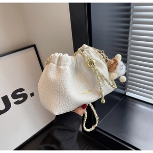 Detailed close-up of white crocodile pattern bucket bag with golden chain and plush charm