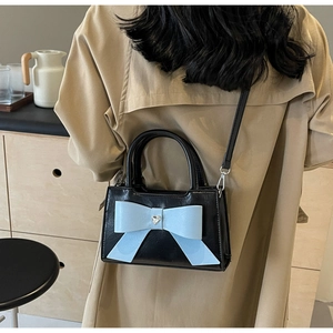 Detail of a black crossbody bag with a large light blue bow and heart crystal on a trench coat
