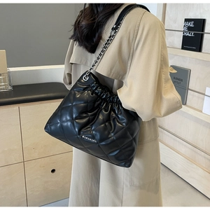 Quilted black leather bucket bag with chain strap worn with a beige trench coat
