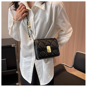 Detail of black quilted crossbody bag with gold lock and metal ball chain charm