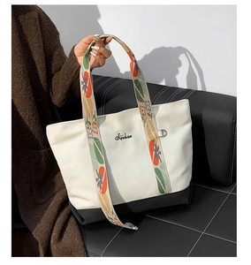Détail du sac cabas en toile avec fond noir et large bandoulière brodée de fleurs