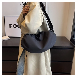 Detail of black crescent crossbody bag showing nylon fabric and textured pleats on model