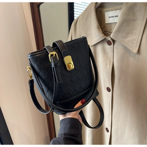 Gros plan sur un sac seau noir avec texture tressée et détails métalliques dorés
