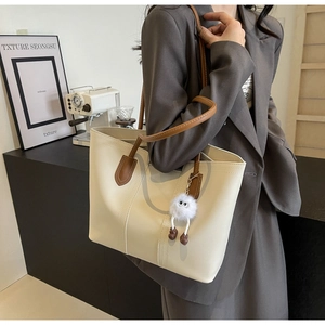 Detail of cream tote bag with brown straps and plush charm worn by model in a cafe
