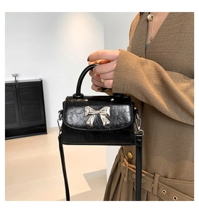 Detail shot of black textured leather bag with a silver metal bow buckle accent