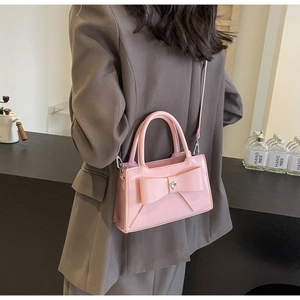 Pink bow handbag with heart metal detail shown on a brown blazer for styling reference