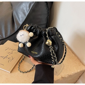 Detail of black crocodile texture bucket bag with gold chain and plush sheep pendant