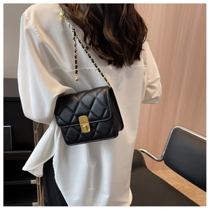 Close-up of black quilted shoulder bag with gold chain strap worn on a model