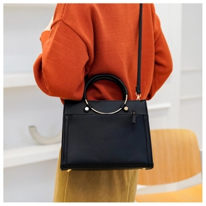 Detailed view of a black structured crossbody bag with a gold metal ring handle and strap