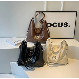 Close-up of three leather Hobo bags in brown, black, and beige with metal M logo and chain strap