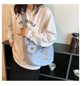 Détail du sac bandoulière croissant bleu clair avec petite pochette ronde et étiquette tissée