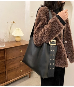 Détail d'un sac seau noir avec bandoulière large et boucle en métal doré brillante