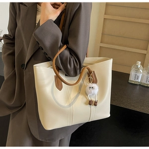 Close-up of beige tote bag with brown straps and cute monster charm on a female model