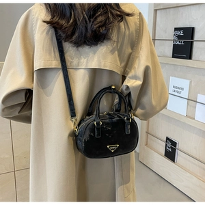 Model wearing black velvet crossbody bag with golden hardware over a brown trench coat