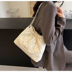 Detail of cream white quilted bucket bag with silver chain strap worn by a model