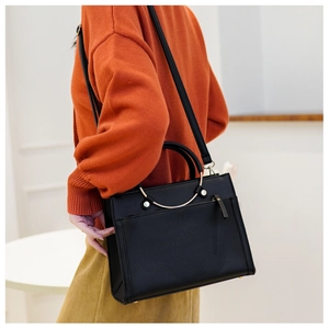 Detail of black structured handbag with gold circular handle worn by model on shoulder