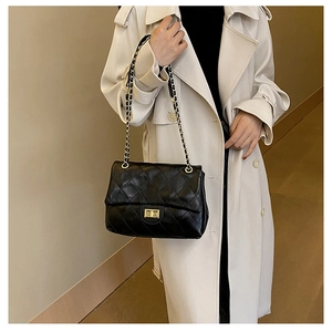 Close-up of black quilted leather crossbody bag with gold chain strap on white coat