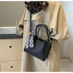 Detail of black lychee grain handbag featuring a decorative checkered silk scarf on handle