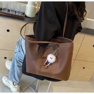 Brown leather tote bag with white contrast stitching and a cute plush doll charm