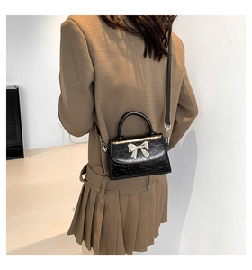 Detail of black glossy wrinkled texture crossbody bag with silver bow buckle on a model