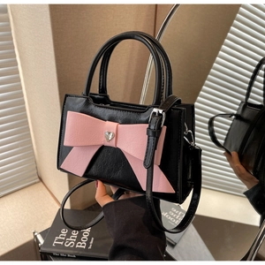 Detail of a black crossbody bag featuring a pink bow with a heart-shaped silver buckle