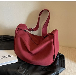 Close-up of burgundy canvas hobo bag with adjustable black strap on a textured surface