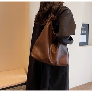 Détail du sac hobo en cuir marron foncé montrant la texture souple et le drapé sur l'épaule