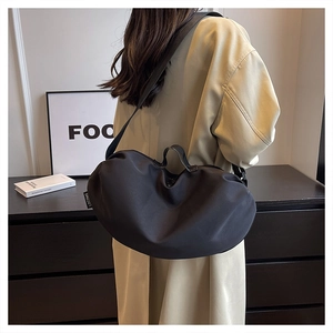 Side view of black nylon crescent bag with adjustable strap worn by model in beige coat