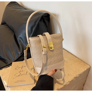 Détail du sac seau beige avec texture diamant et fermoir doré sur socle en pierre