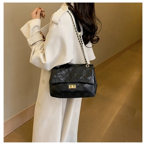 Model wearing a black quilted leather crossbody bag with a gold chain strap and turn-lock