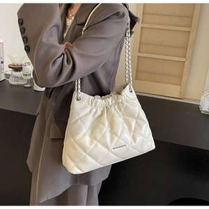 White quilted bucket bag with silver chain strap worn by a model in a brown suit