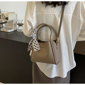Detail of khaki bucket bag featuring litchi texture and stylish plaid scarf handle