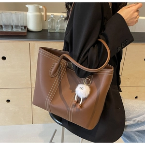 Brown leather tote bag with white contrast stitching and plush monster charm detail