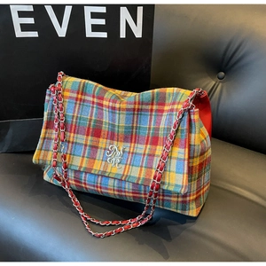 Detail shot of colorful woven plaid tote with metal logo and chain strap on leather seat