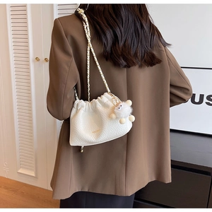 Detail of white pleated cloud bag with litchi texture, gold chain and plush ball charm