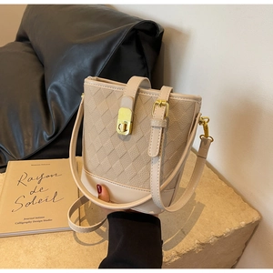 Détail du sac seau beige montrant la texture du cuir grainé et le fermoir doré rotatif