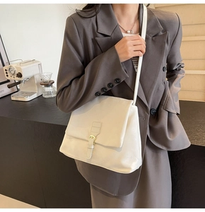 Detail view of a cream leather tote bag featuring a minimalist flap and metal buckle