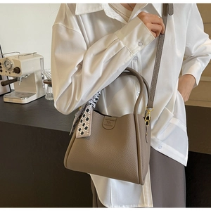 Detail of taupe leather bucket bag with silk scarf handle and embossed logo accent