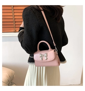 Detail of pink small square bag featuring a metallic silver bow accent and slim strap