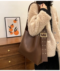 Détail d'un sac seau en cuir marron avec large bandoulière et boucle en métal doré